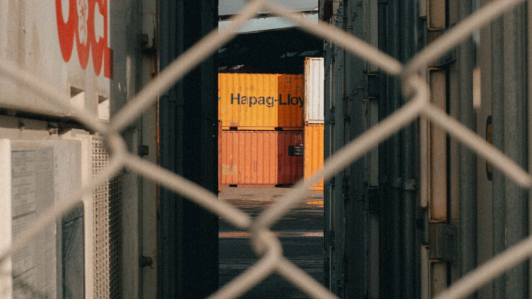 Containers behind a chain linked fence, symbolizing detention.
